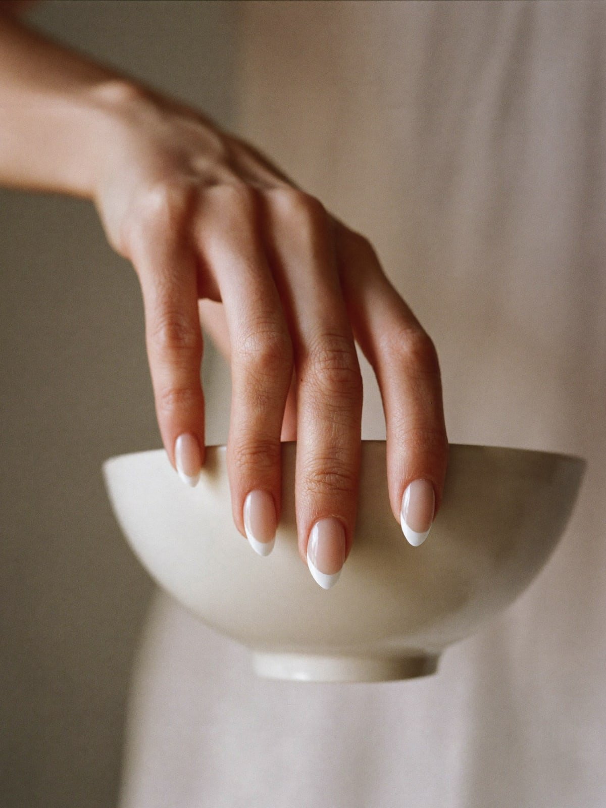 Micro French press-on nails worn on hand — Medium almond · Sheer nude, hairline tip